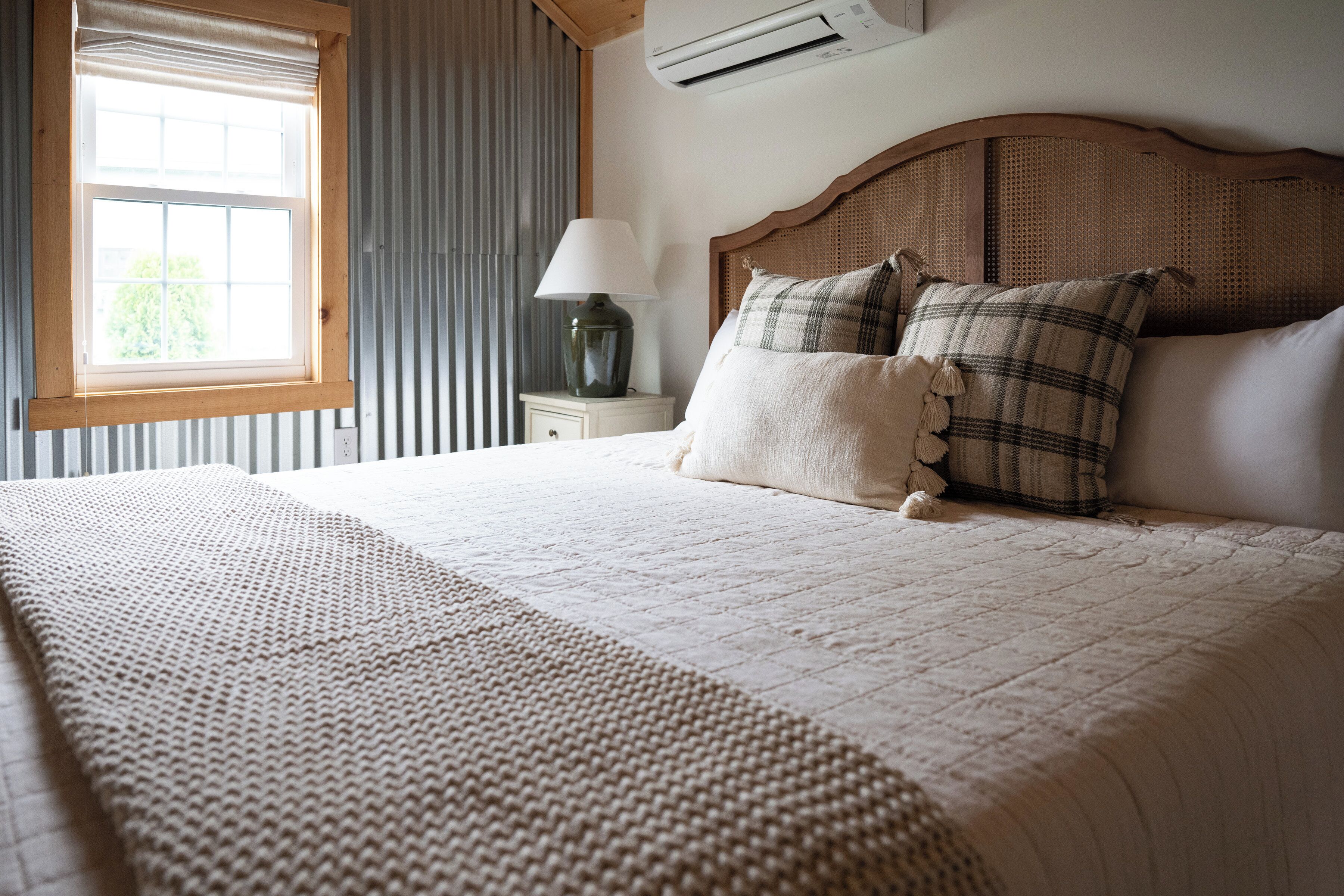 Een keurig opgemaakt bed met hoofdeinde, een bedlampje en een raam met gordijnen.