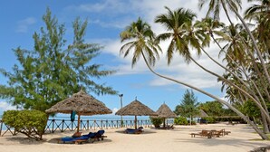 A beach with thatched umbrellas, lounge chairs, and palm trees.