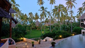 A resort with a pool, palm trees, and thatched-roof buildings.