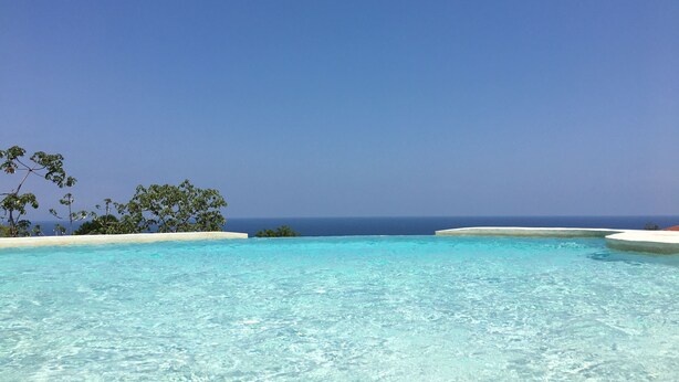 A clear blue sky above a pool with a view of the ocean.
