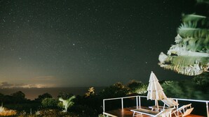 A deck with lounge chairs and an umbrella, overlooking a night sky filled with stars.