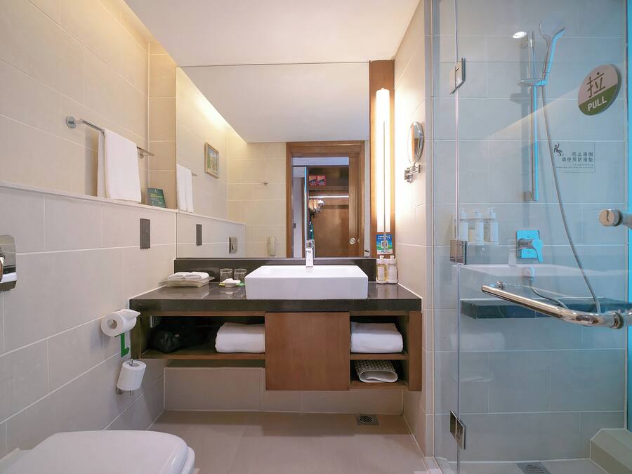 Une salle de bain moderne comprenant un lavabo, un miroir, un porte-serviettes, des toilettes et une douche séparée par une paroi en verre.