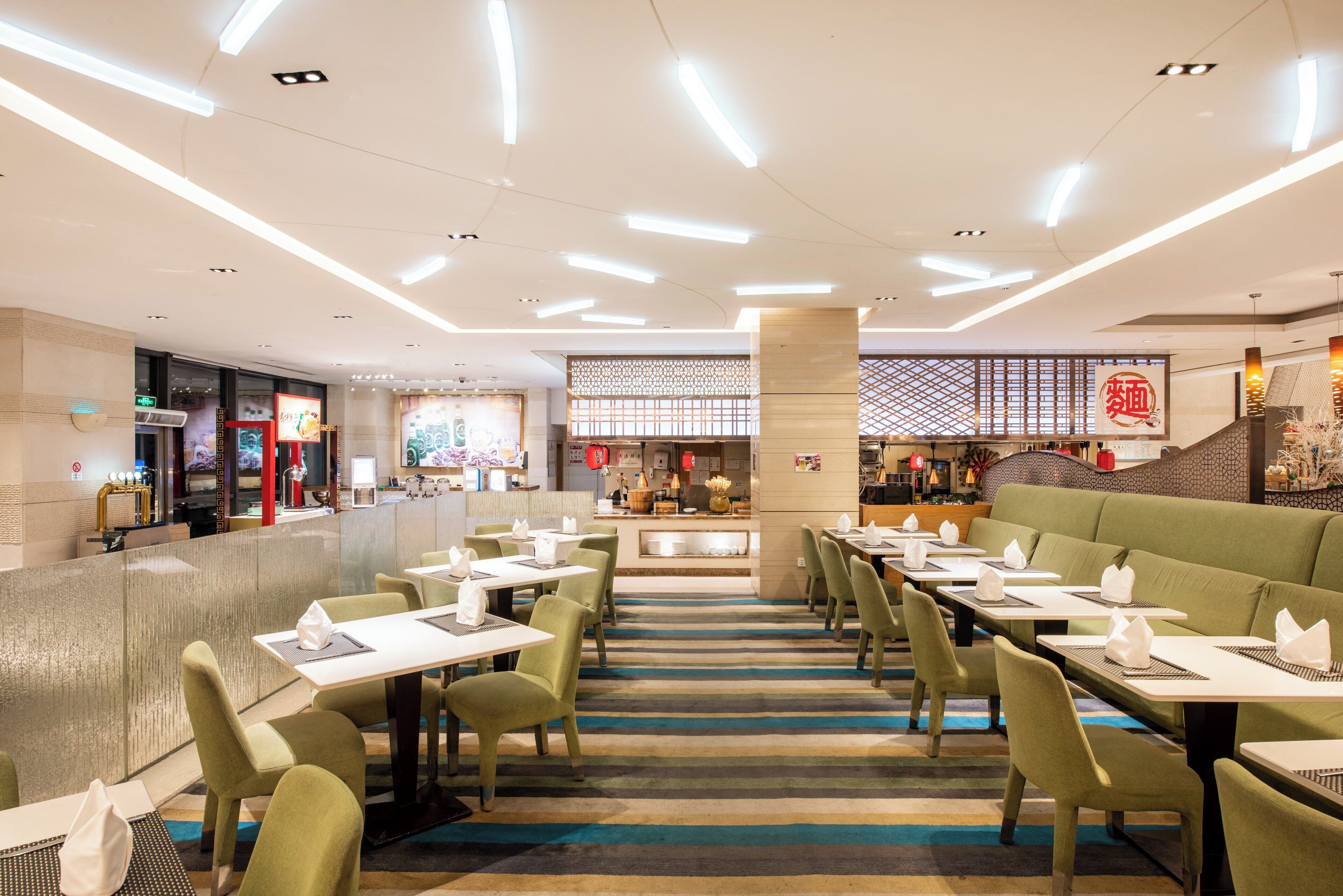 Een modern restaurantinterieur met meerdere eettafels en stoelen, een bar en een decoratieve wand met een geometrisch patroon.