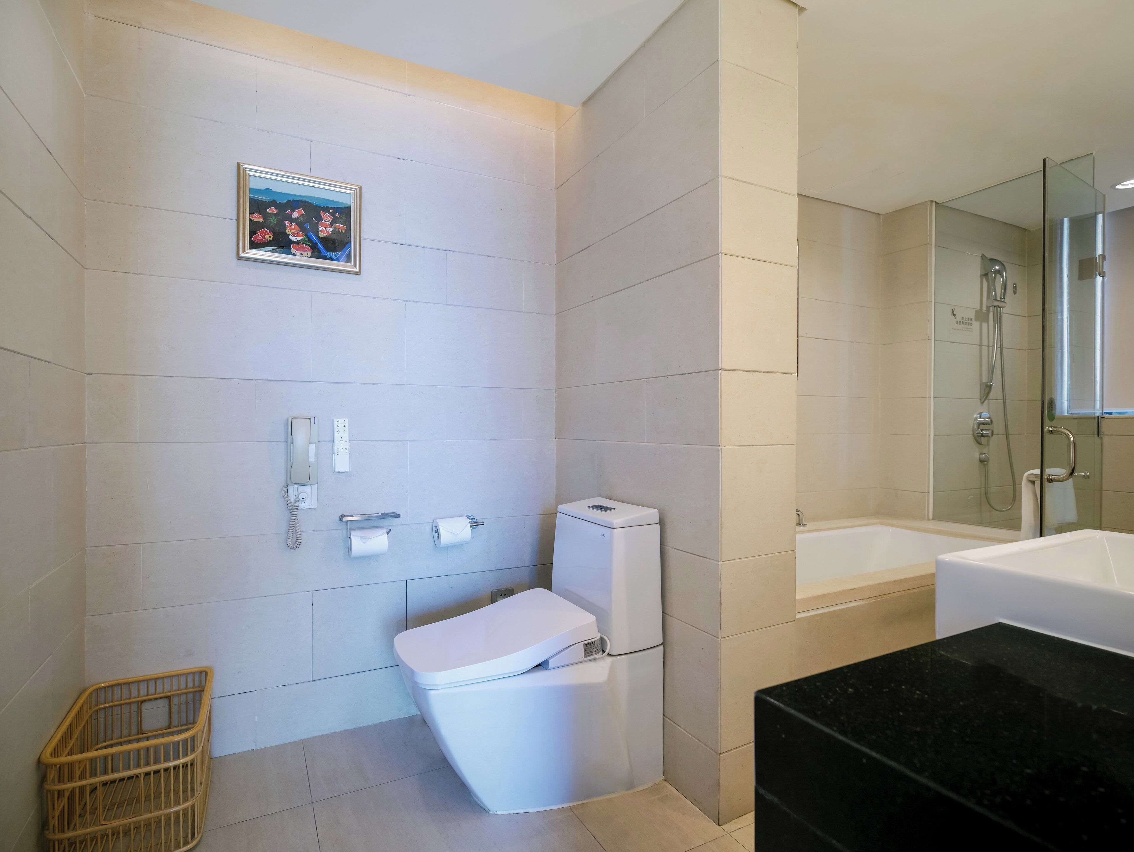 A bathroom with a toilet, a shower, a sink, a mirror, and a framed picture on the wall.