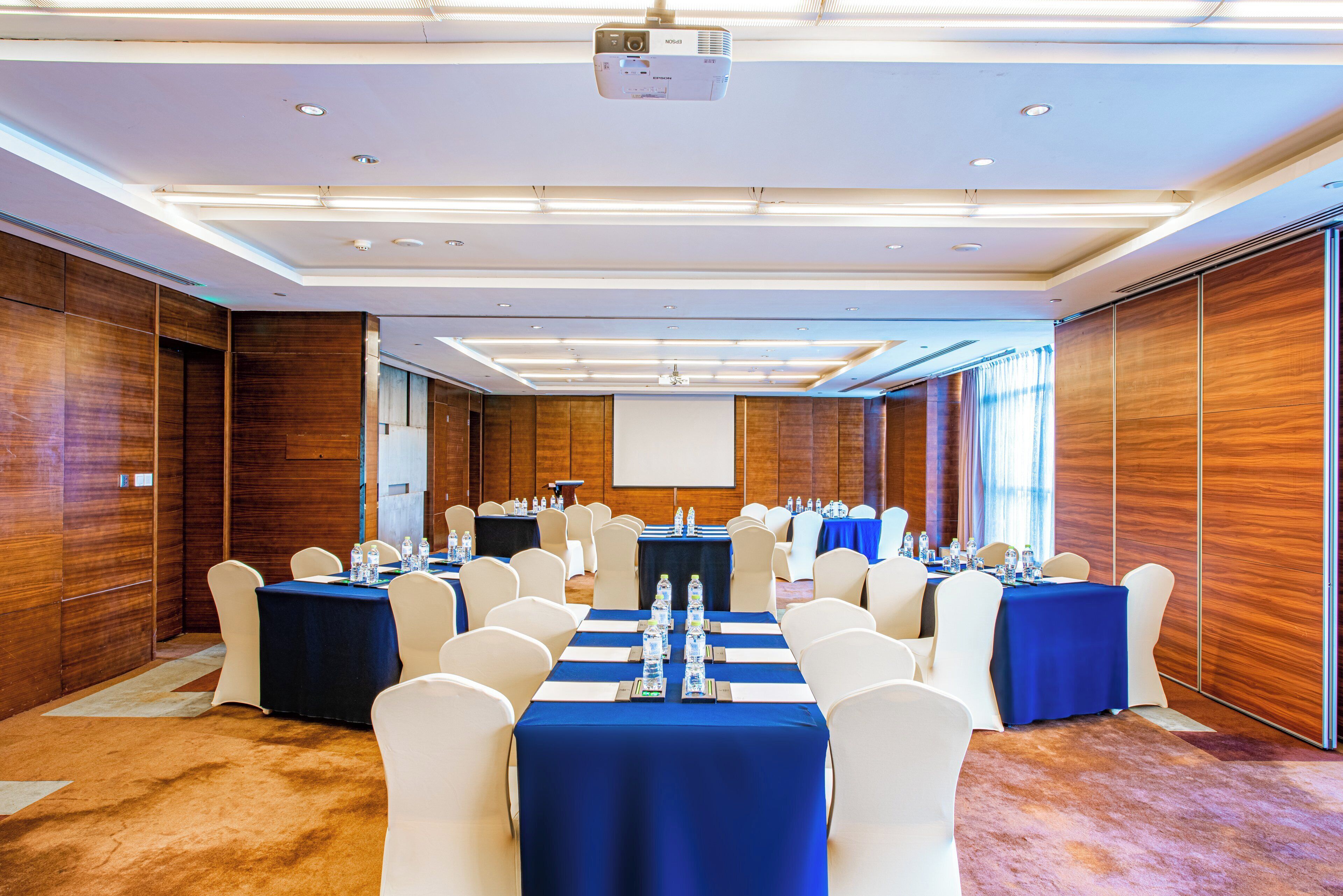 A conference room with multiple tables, chairs, and a projector screen.