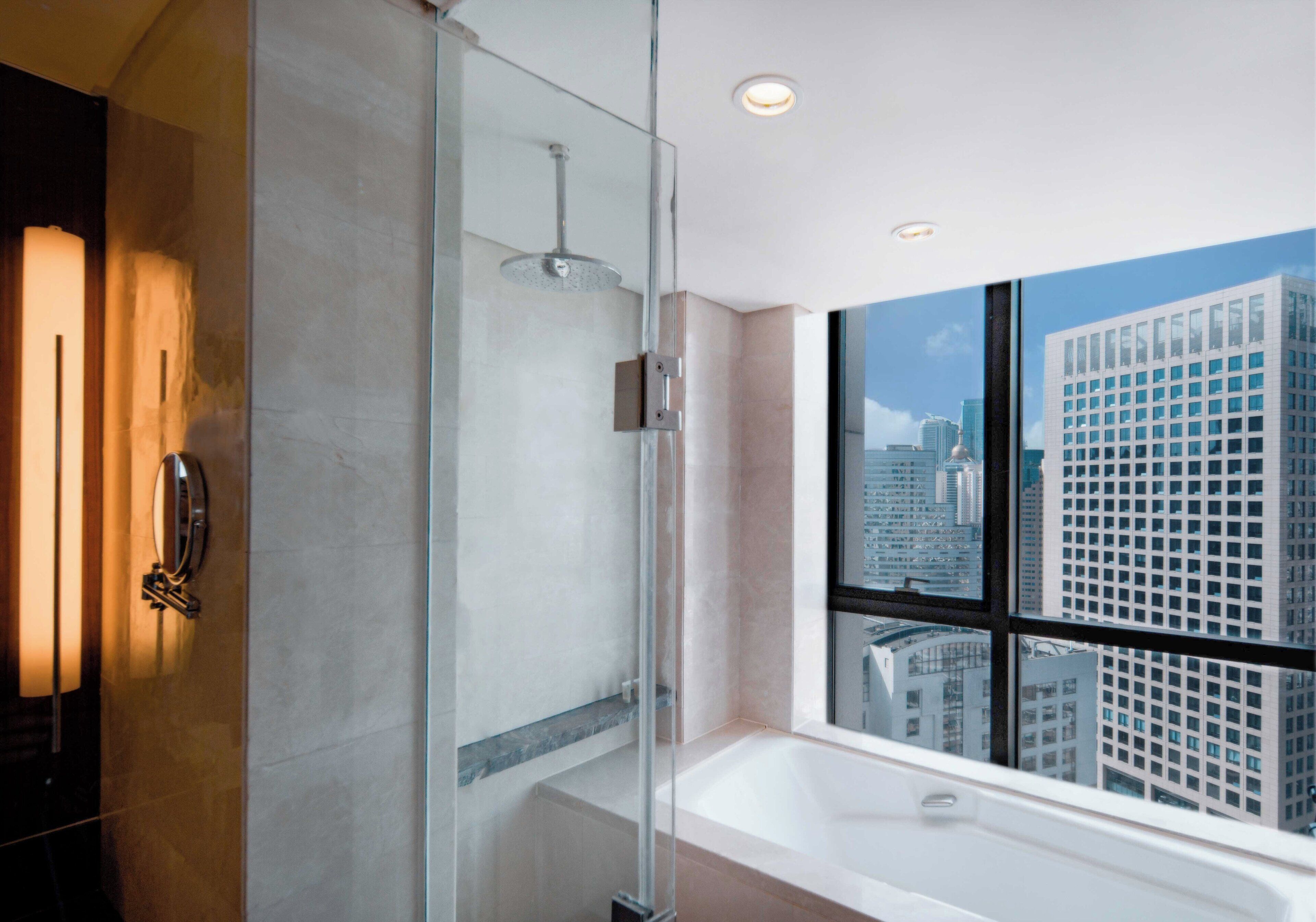 Een moderne badkamer met een douchecabine van glas, een groot bad en een stadszicht door een groot raam.