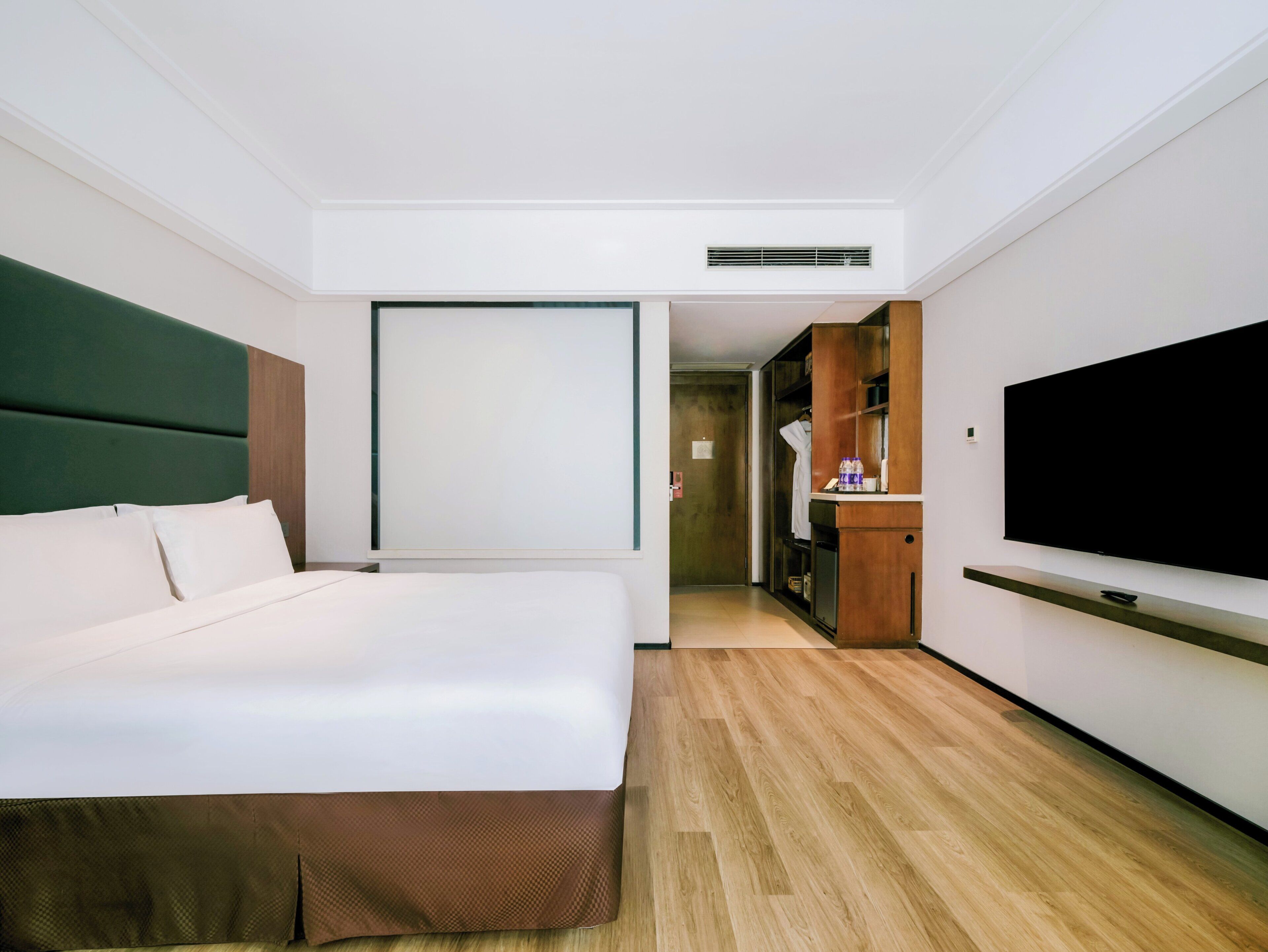 A hotel room with a bed, a television, a wardrobe, and a mirror.