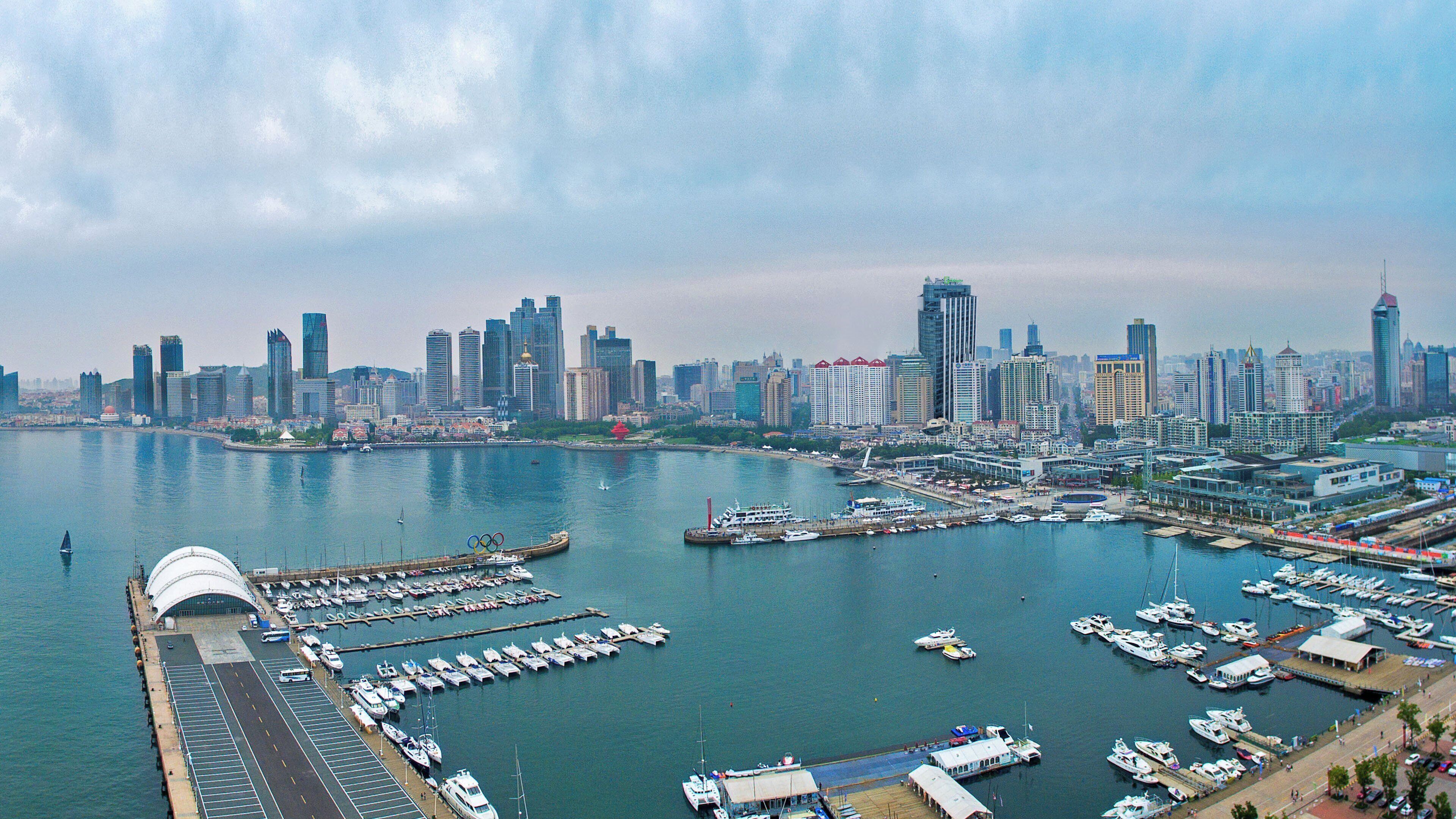 A marina with boats docked, a city skyline in the background, and a large white dome structure.