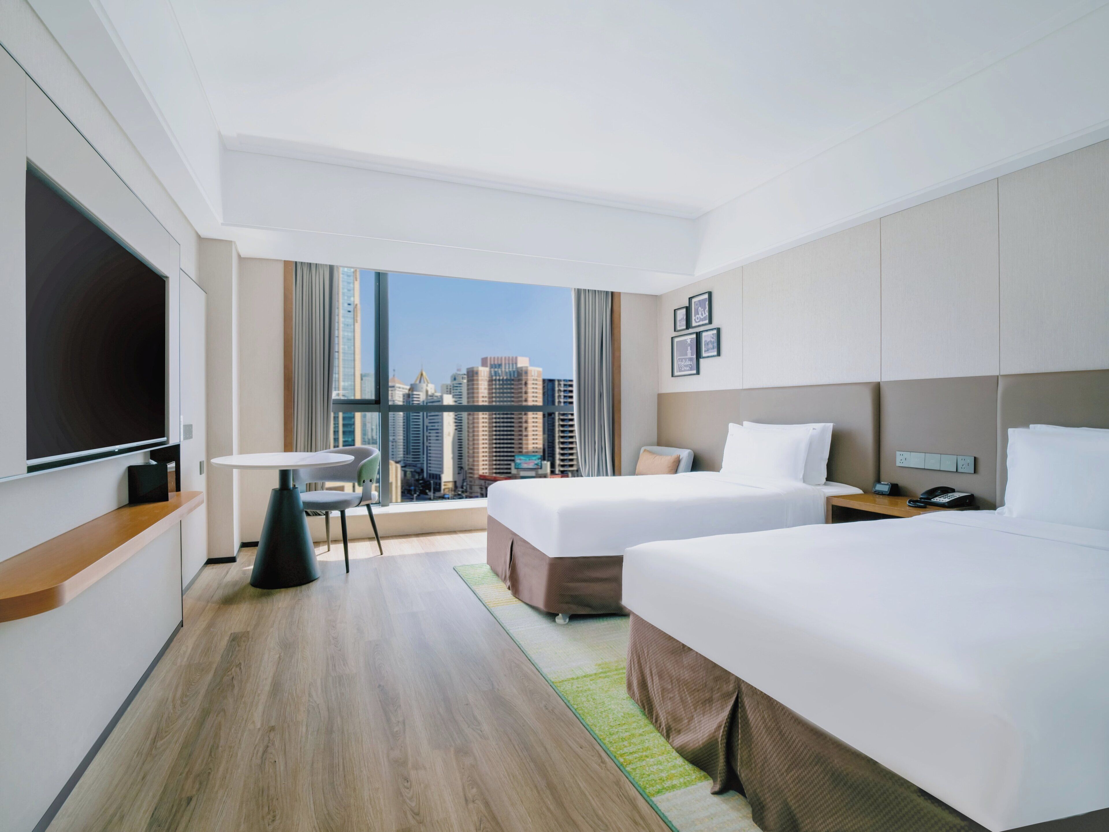 A hotel room with two beds, a TV, a small table, and a view of a cityscape.