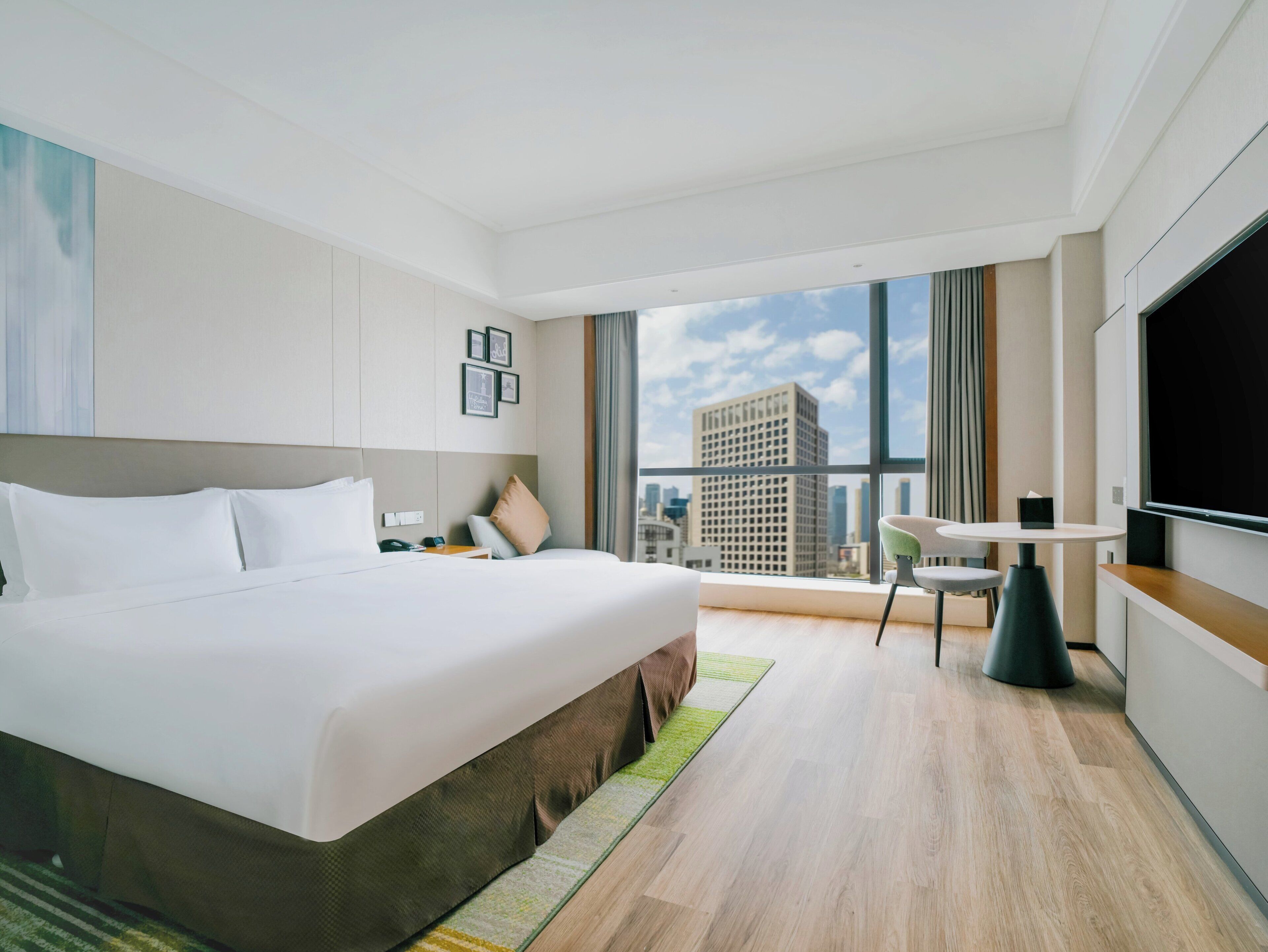 A modern hotel room with a large bed, a desk with a chair, a TV, and a city view.