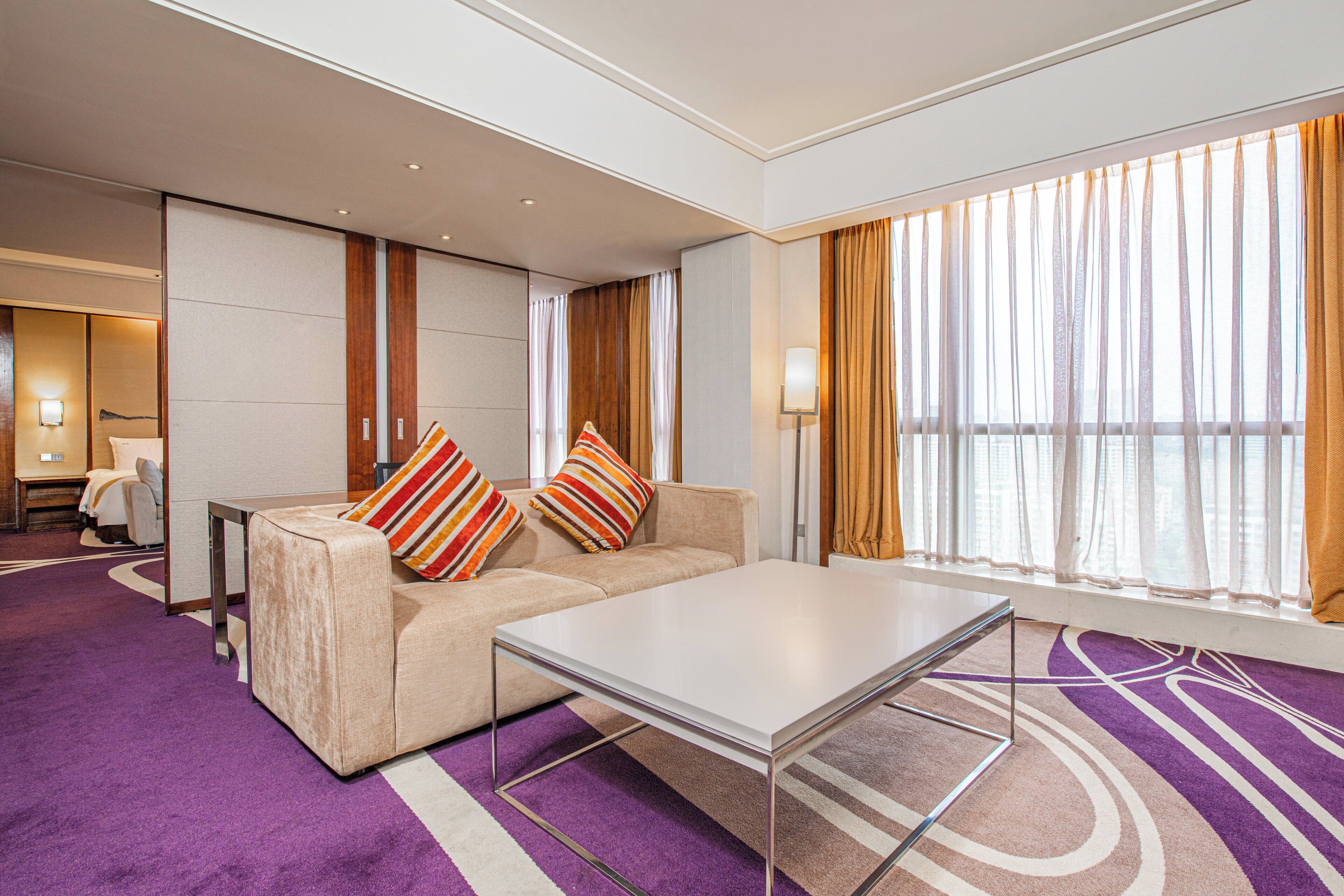 A modern hotel room with a sofa, a coffee table, and a large window with curtains.