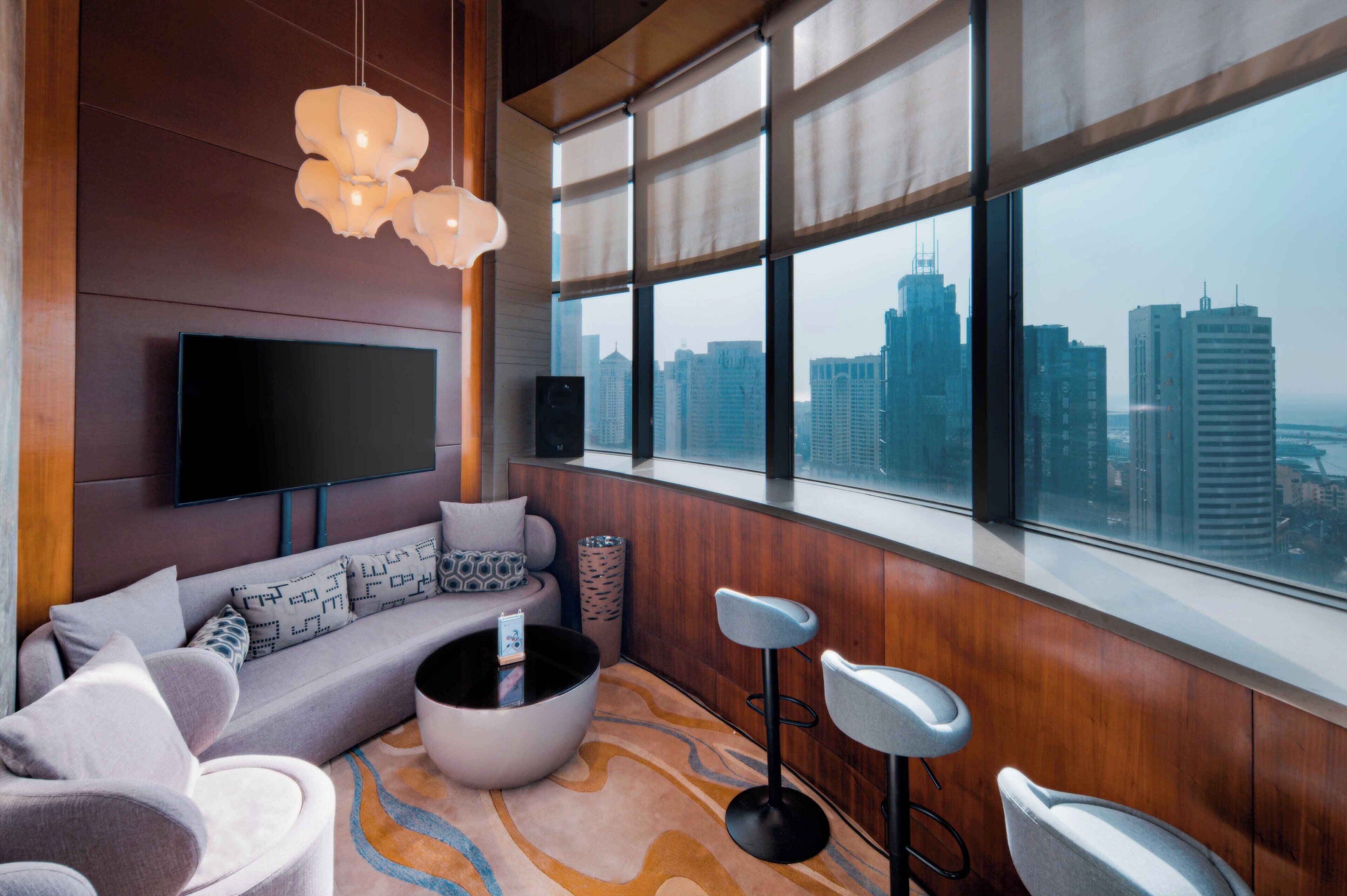 A modern living room with a large window, a sofa, a coffee table, and a TV mounted on the wall.