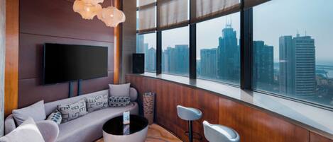 A modern living room with a large window, a sofa, a coffee table, and a TV mounted on the wall.