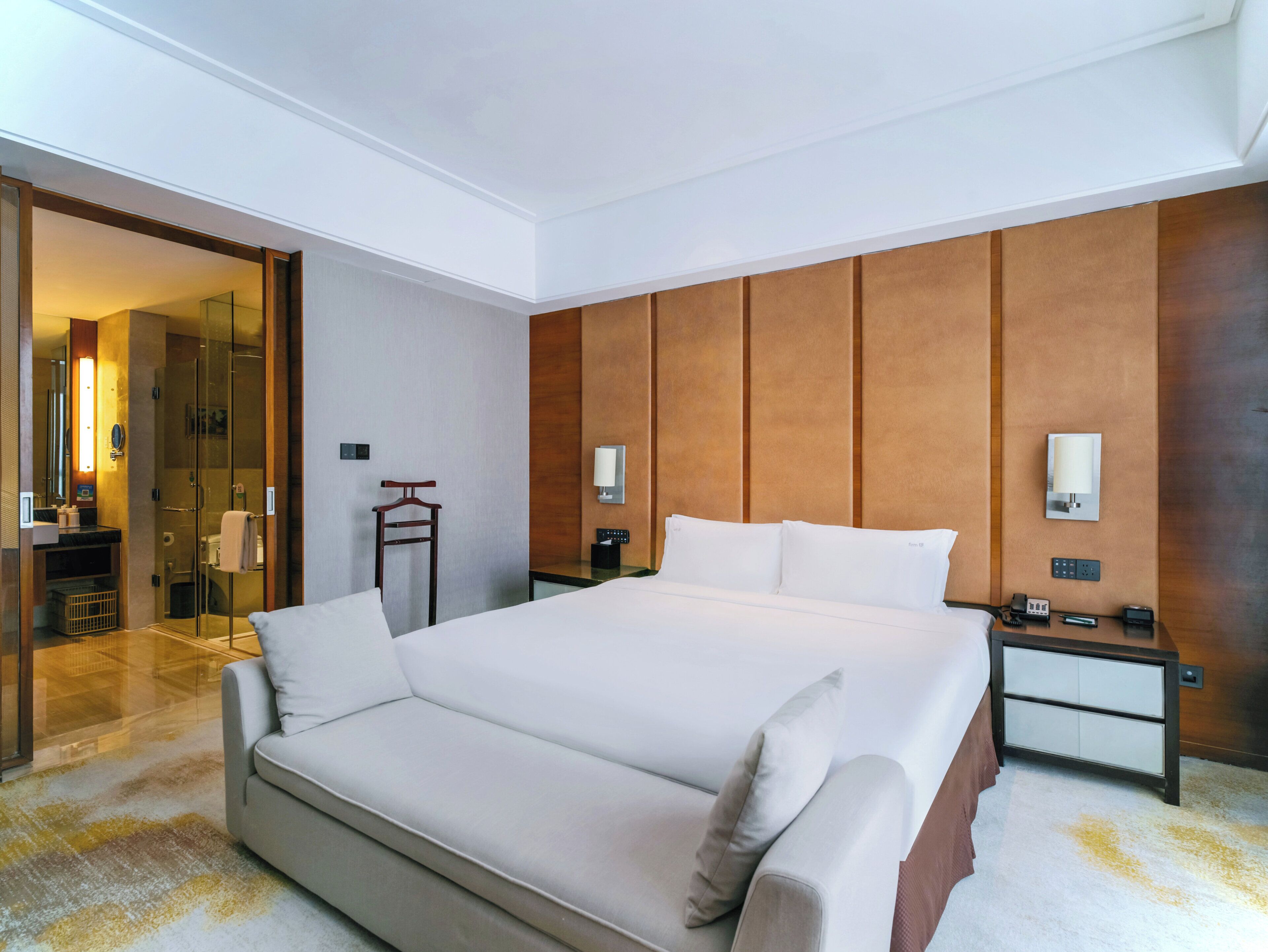 A hotel room with a large bed, bedside tables, a mirror, and a shower area.