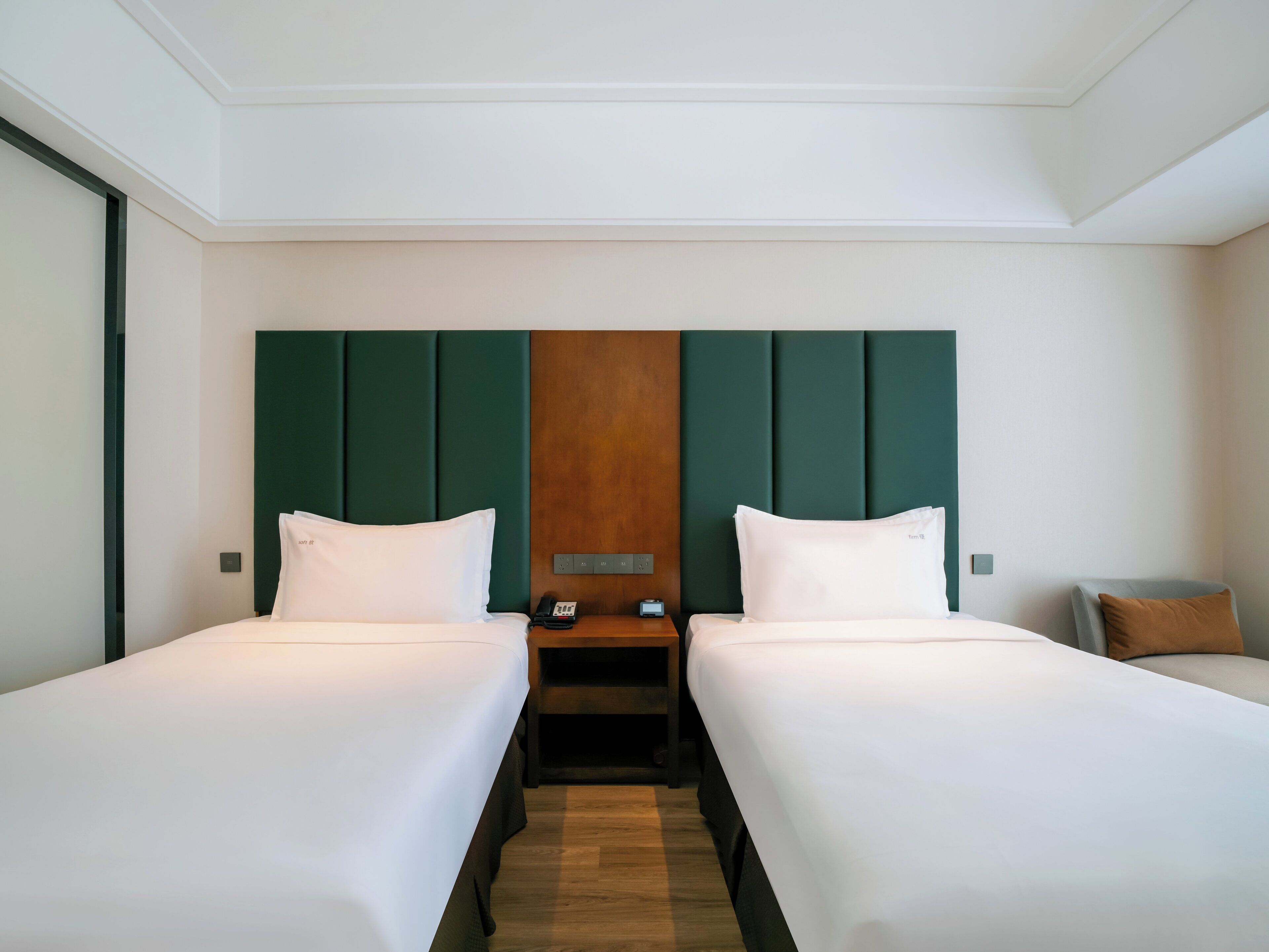 A hotel room with two single beds, a wooden headboard, a bedside table with a phone, and a nightstand.