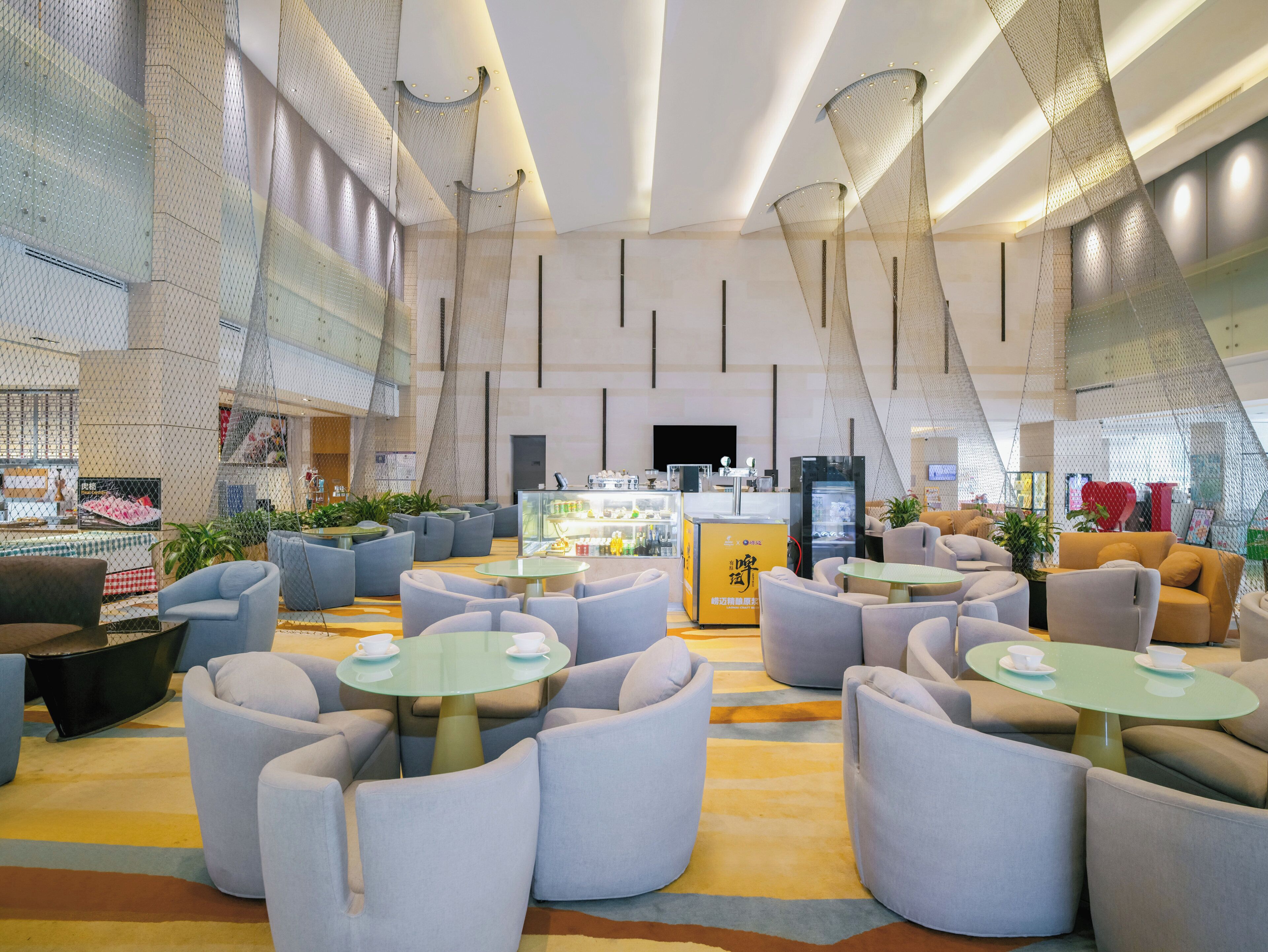 A modern hotel lobby with seating areas, a bar, and a large screen.