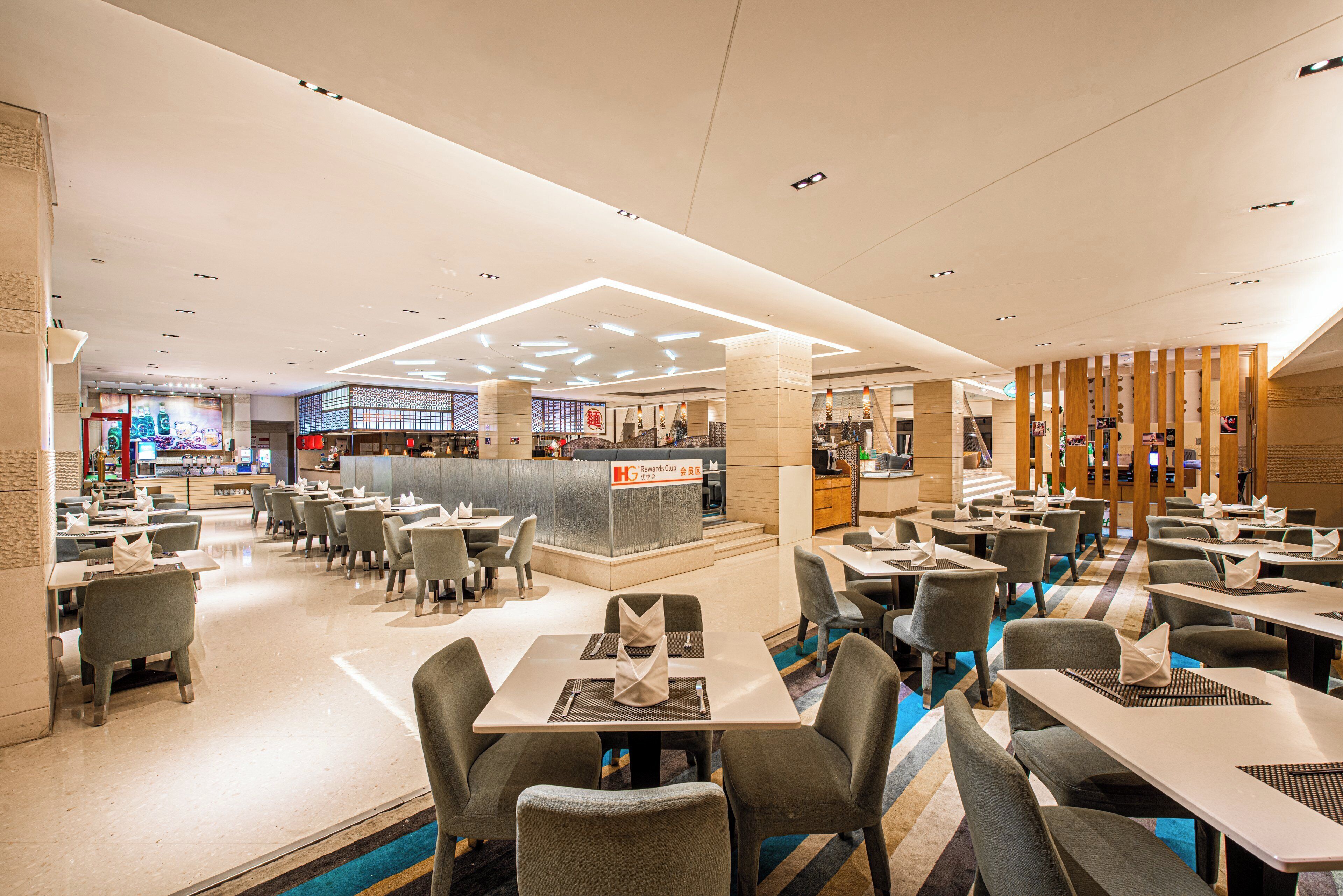 A modern hotel restaurant with multiple dining areas, a central bar, and a reception desk.