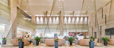 Een ruime lobby met moderne zitplaatsen, potplanten en een uniek plafondontwerp.
