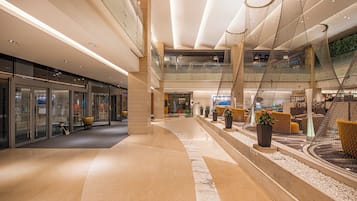 A spacious indoor area with a curved marble floor, glass doors, and a seating area with yellow chairs.