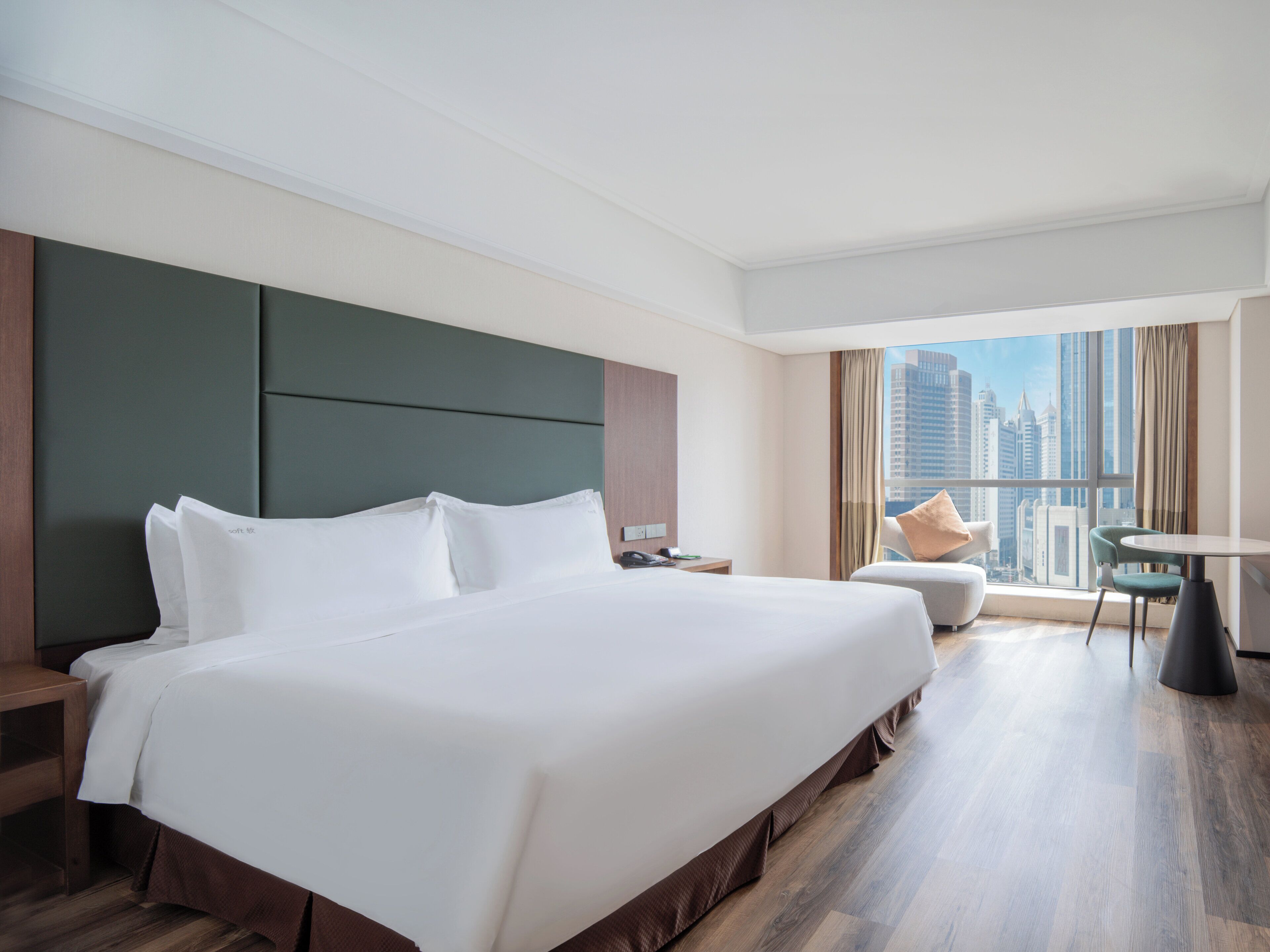Habitación de hotel con una cama grande, una mesita, una silla y vistas a la ciudad.
