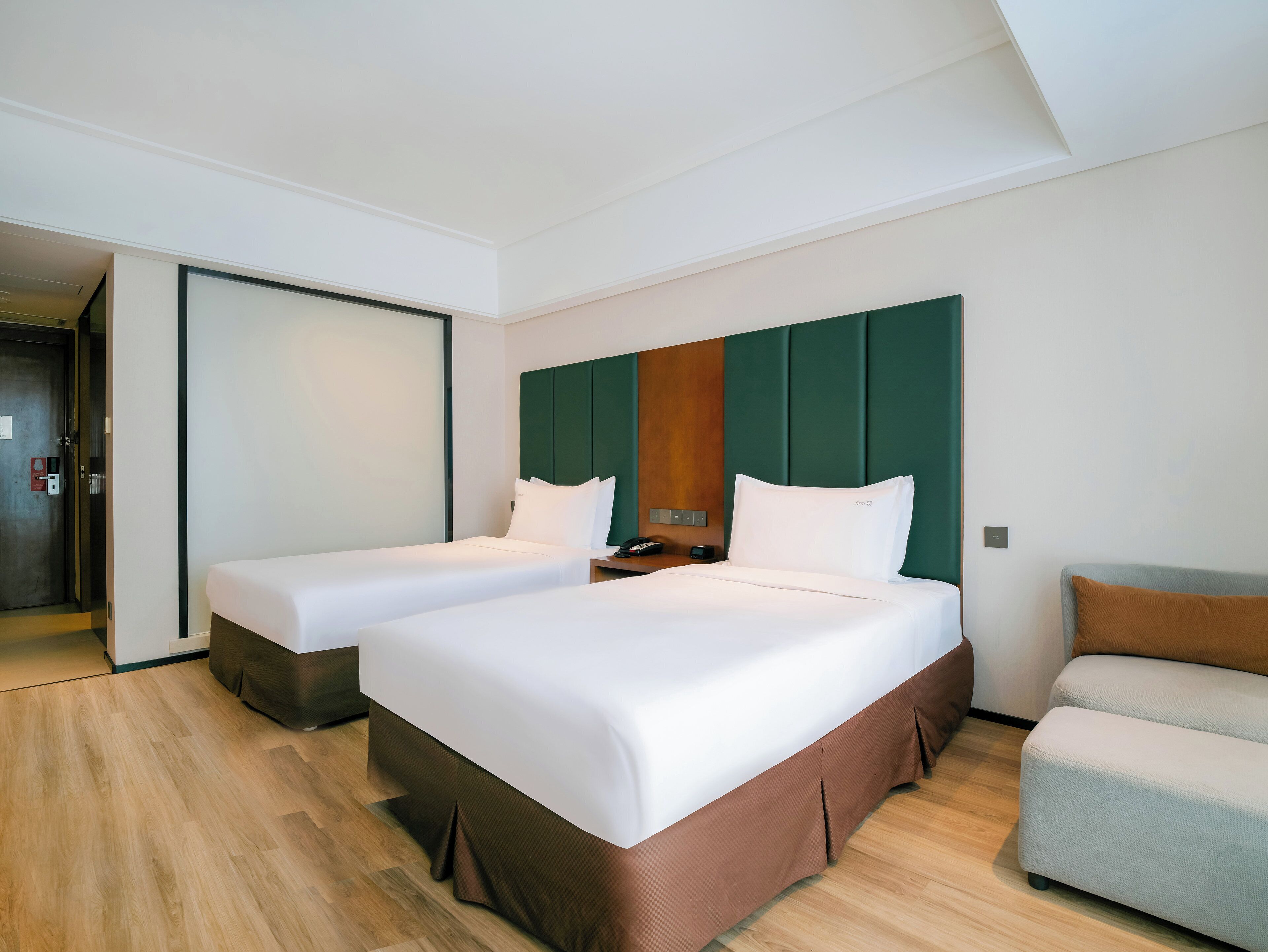 Habitación de hotel con dos camas, un sofá, piso de madera y una pared verde decorativa.