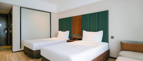 Habitación de hotel con dos camas, un sofá, piso de madera y una pared verde decorativa.