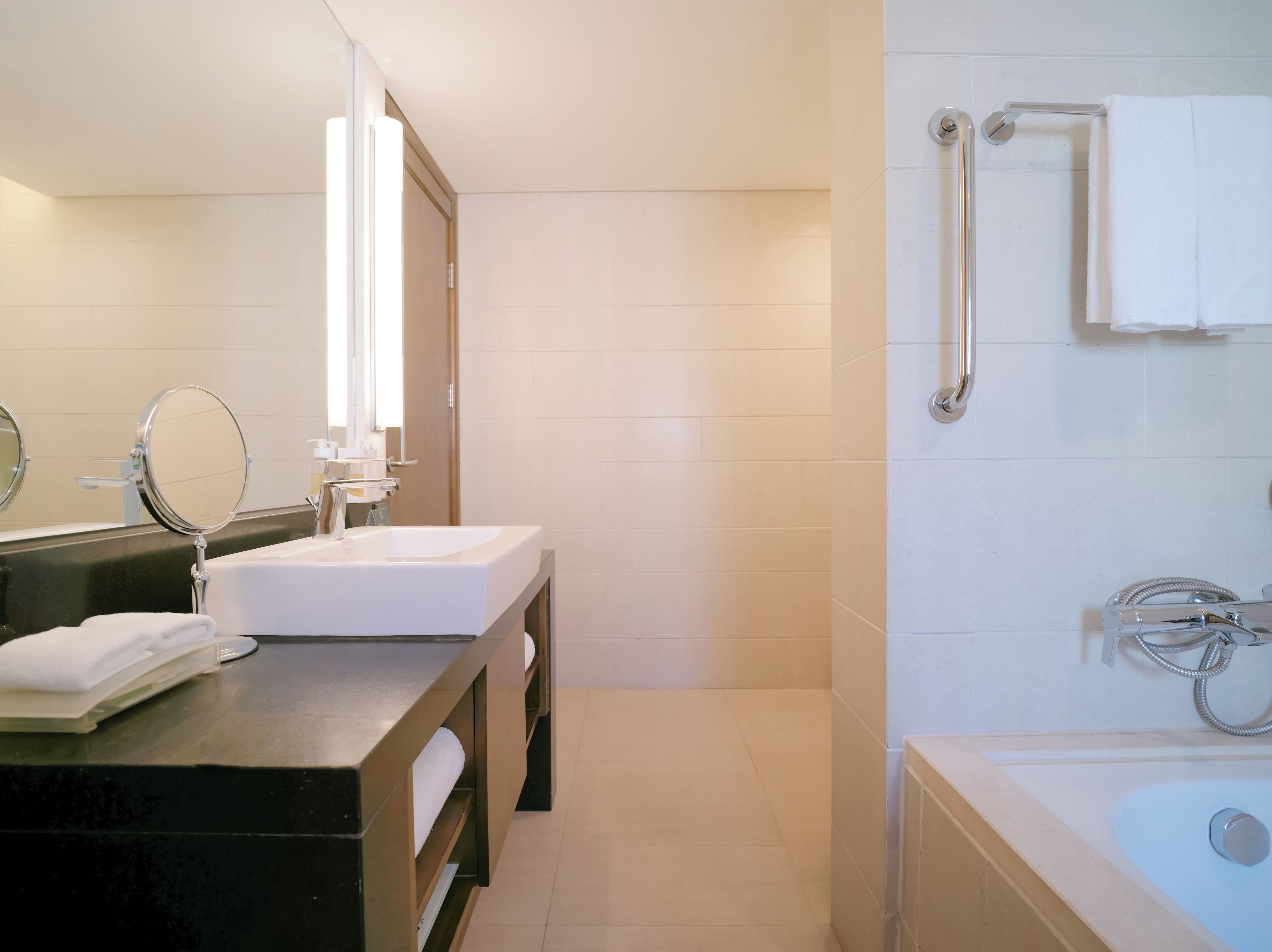 A modern bathroom with a large mirror, two sinks, a bathtub, and a shower with grab bars.