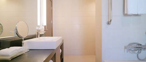 A modern bathroom with a large mirror, two sinks, a bathtub, and a shower with grab bars.