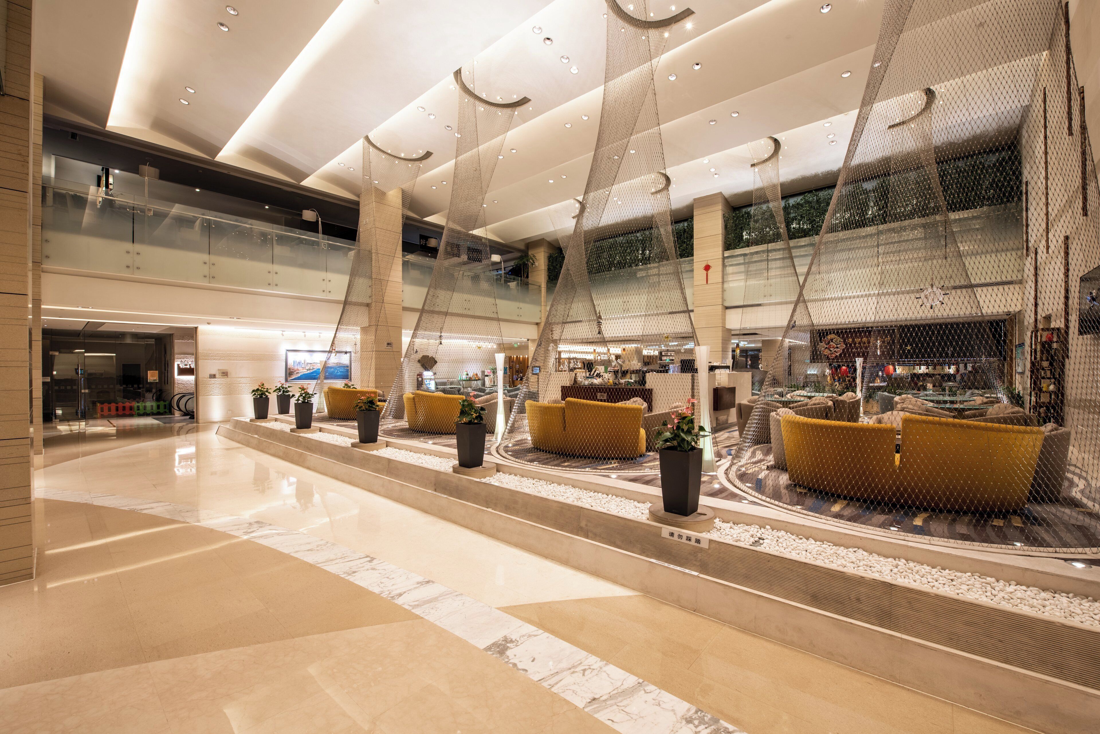 A spacious lobby with a high ceiling, modern lighting, and a seating area with yellow cushions.