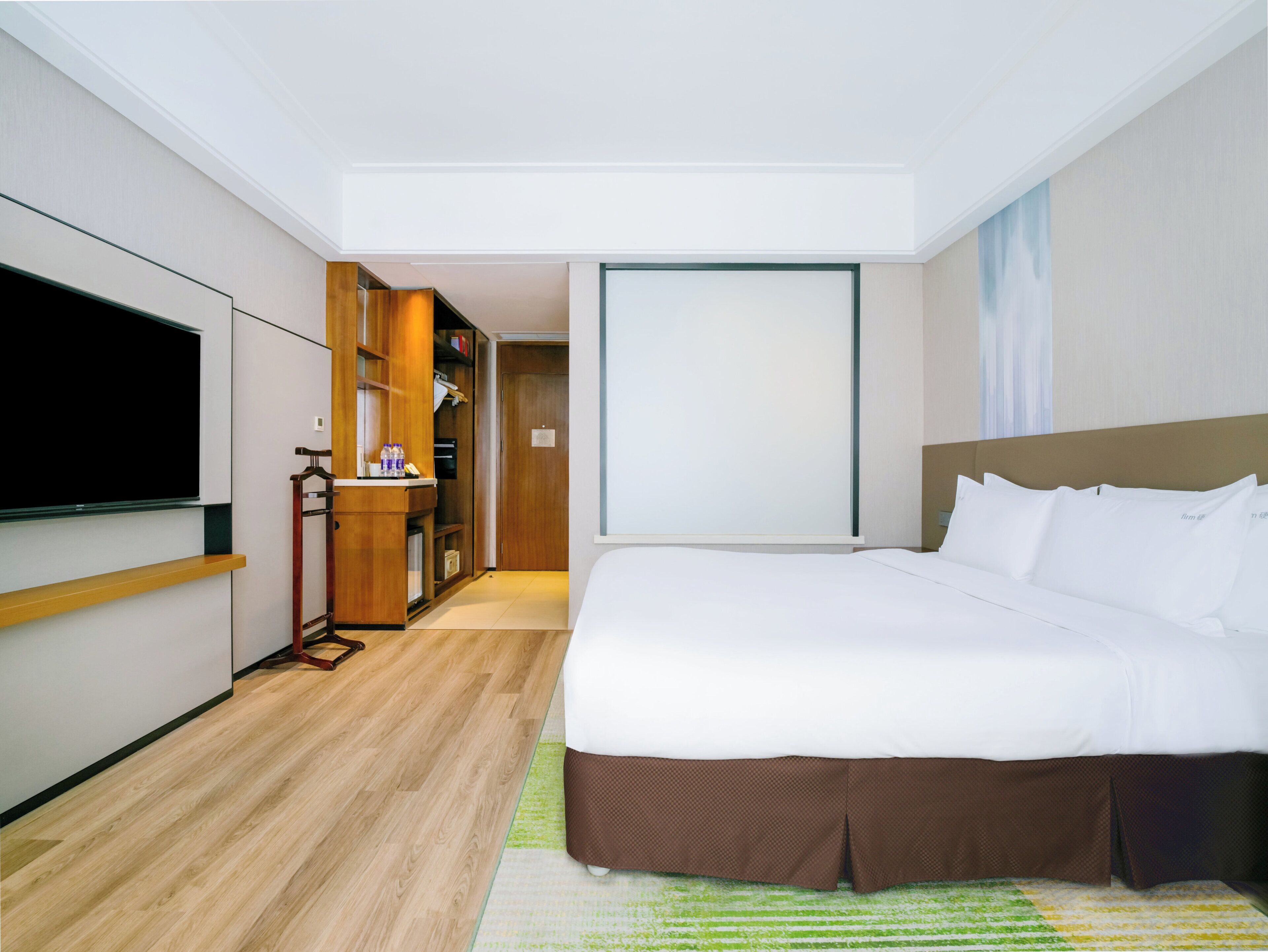 Una camera d'albergo con un letto, una TV, un armadio e una porta che dà su un corridoio.