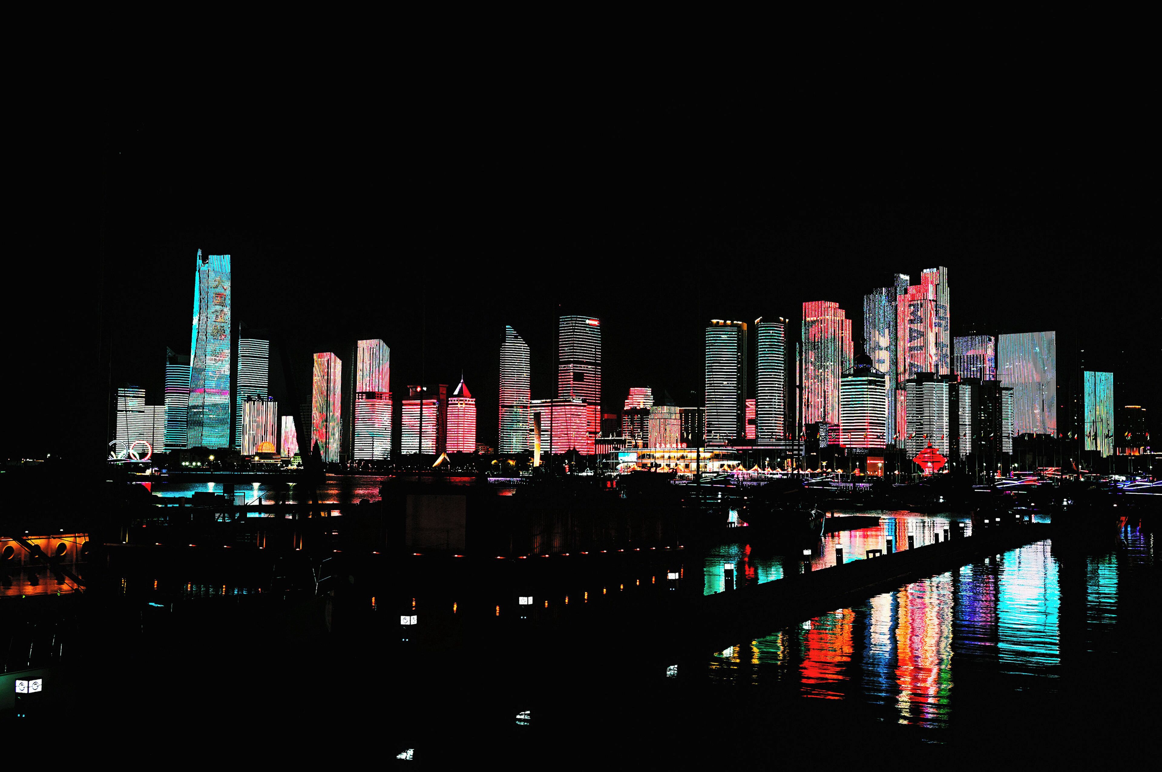 A nighttime city skyline with illuminated buildings reflecting on water.