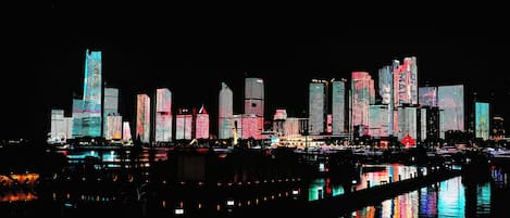 A nighttime city skyline with illuminated buildings reflecting on water.