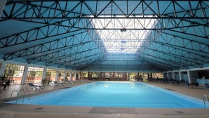 An indoor swimming pool with a high ceiling and skylight, surrounded by lounge chairs and tables. - Imperial Botanical Beach Hotel (Entebbe)