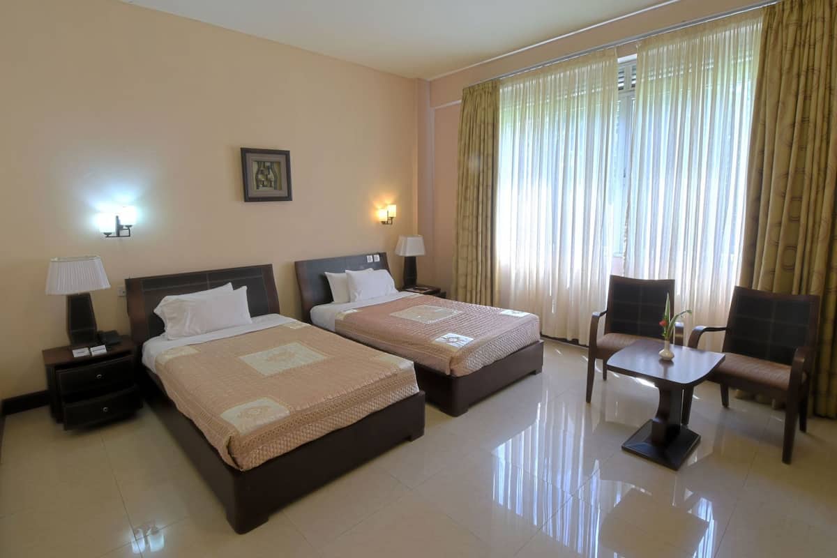 Una habitación de hotel con dos camas, una mesita, una silla y un ventanal con cortinas.