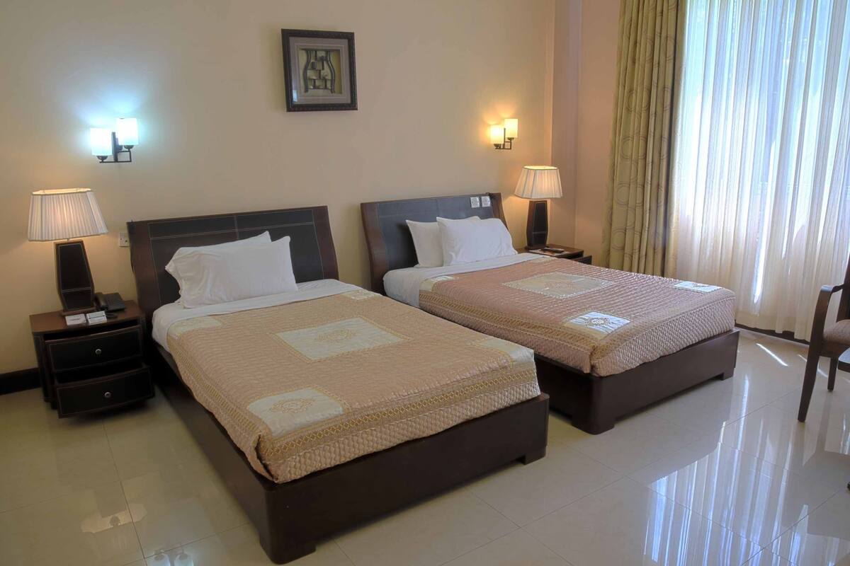 Habitación de hotel con dos camas, cada una con cabecera, lámparas de noche y mesita de noche con teléfono y una pequeña mesa.