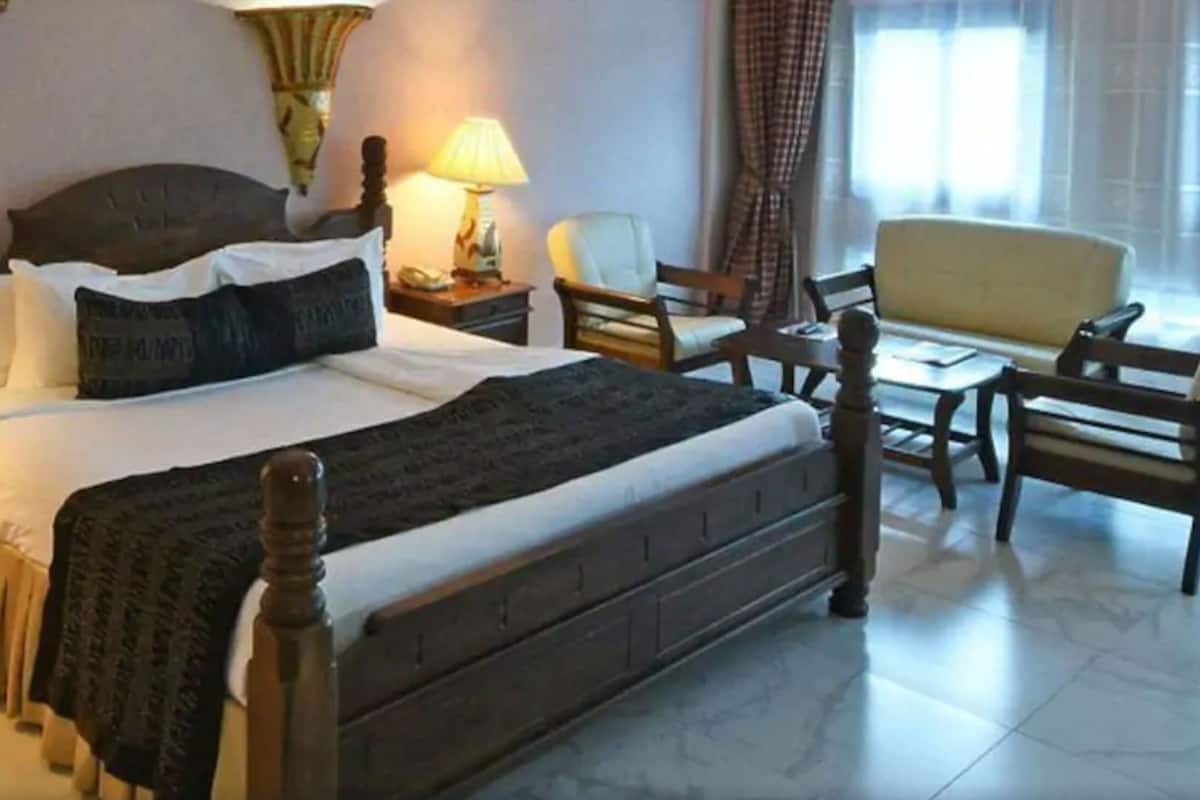 Una habitación de hotel con una cama grande, dos mesitas de noche con lámparas, una silla y una pequeña mesa.