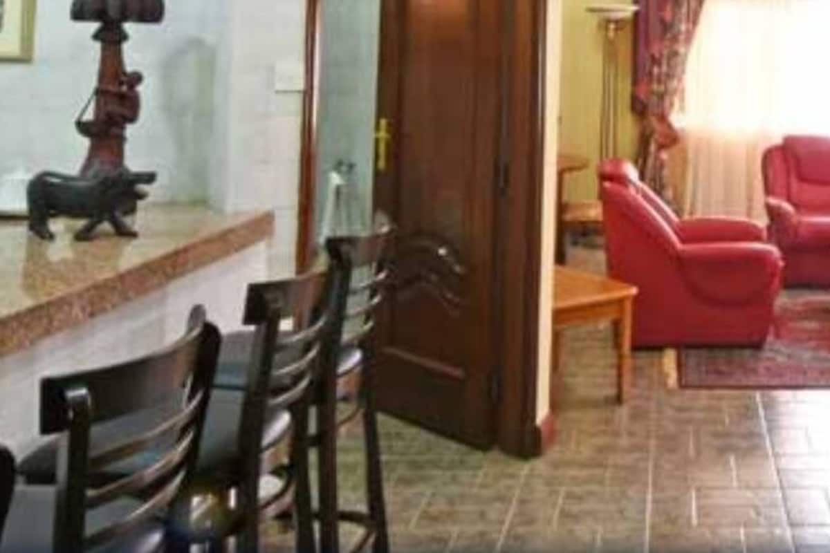 Una sala de estar con un sofá rojo, una mesa de centro de madera y un tapete estampado. Hay dos sillones y una mesita en la esquina.