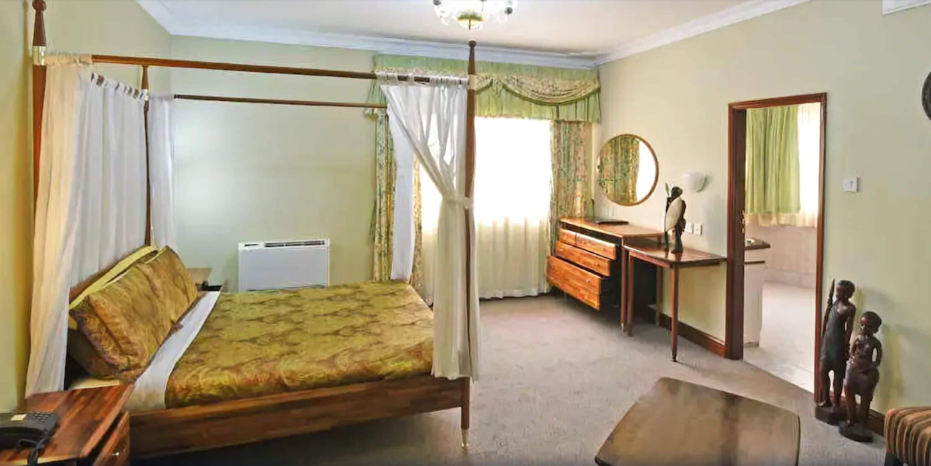 A bedroom with a four-poster bed, a wooden dresser, a mirror, and a small statue.