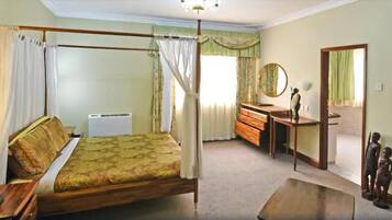 A bedroom with a four-poster bed, a wooden dresser, a mirror, and a small statue.