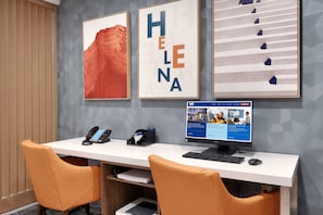 A hotel reception desk with a computer, phone, and framed artwork.