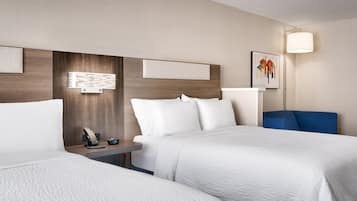 A hotel room with two beds, a bedside table with a phone and a clock, a wall-mounted light, and a painting.
