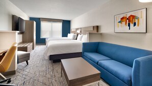 Ein Hotelzimmer mit zwei Betten, einem blauen Sofa, einem Holztisch, einem Fernseher und einem Gemälde an der Wand.