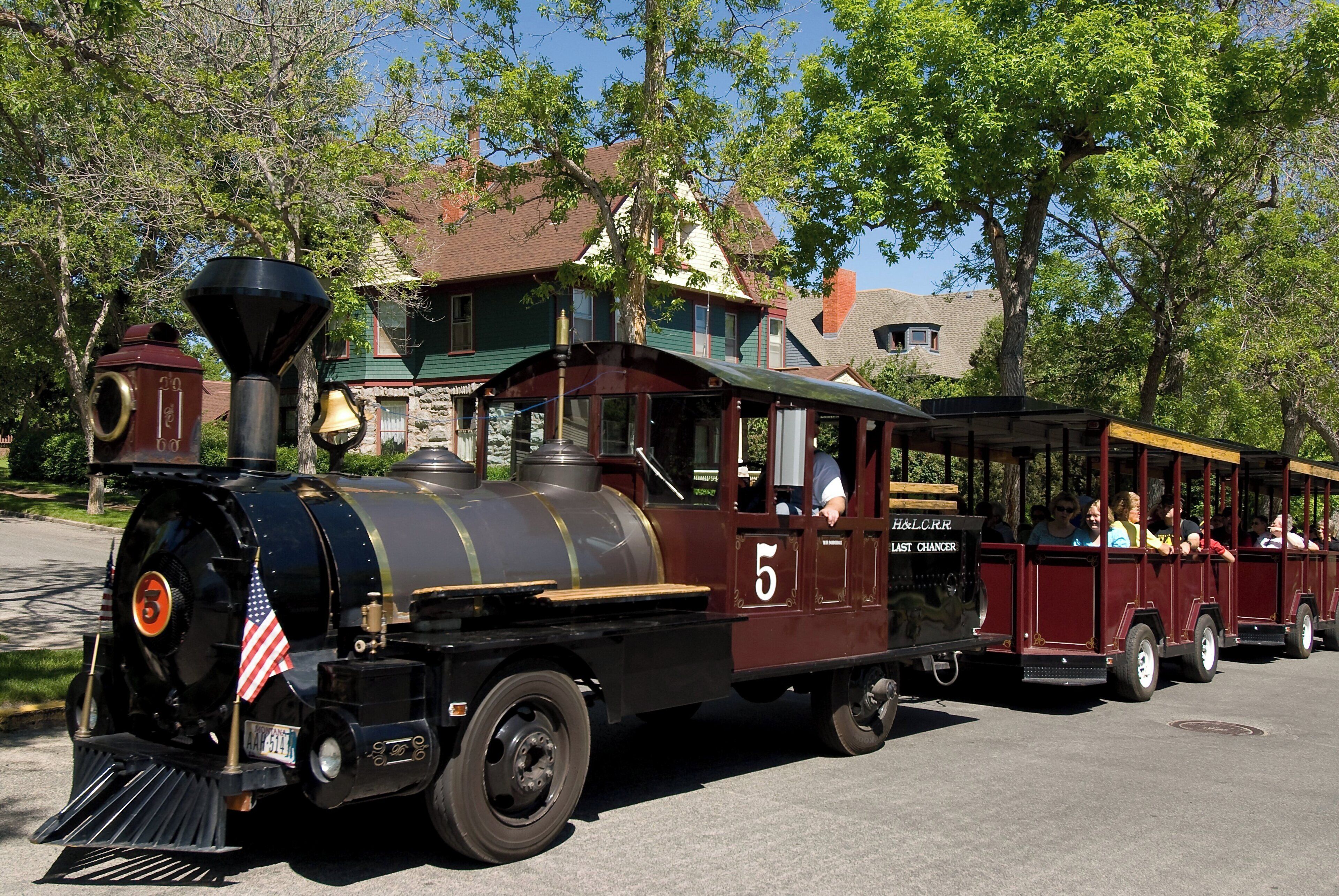 A vintage steam locomotive with a number 5, passengers, and a vintage trolley car.