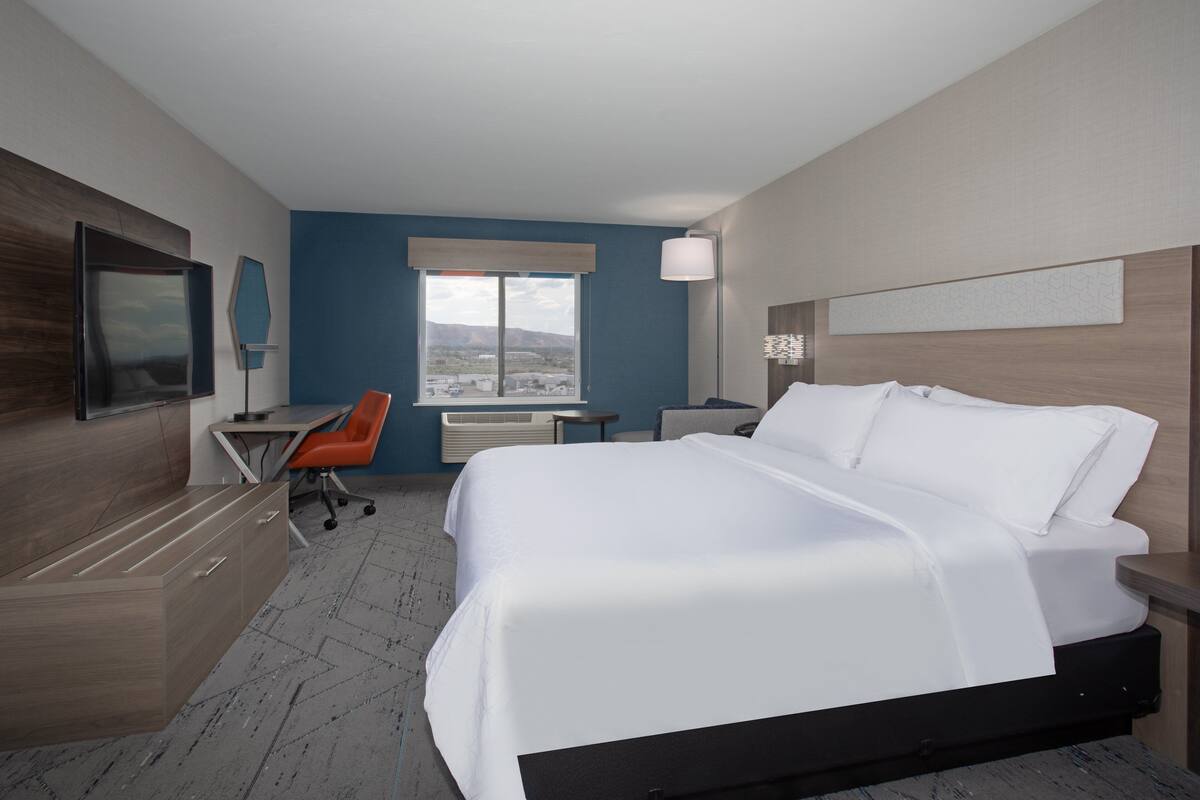 A hotel room with a bed, desk, chair, and a large window with a view.