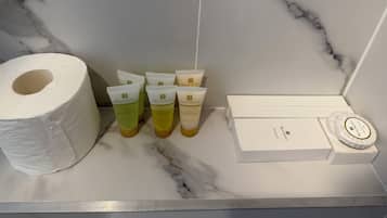 A bathroom with a marble floor, a roll of toilet paper, and several toiletries including body wash, shampoo, conditioner, and a box of toiletries.