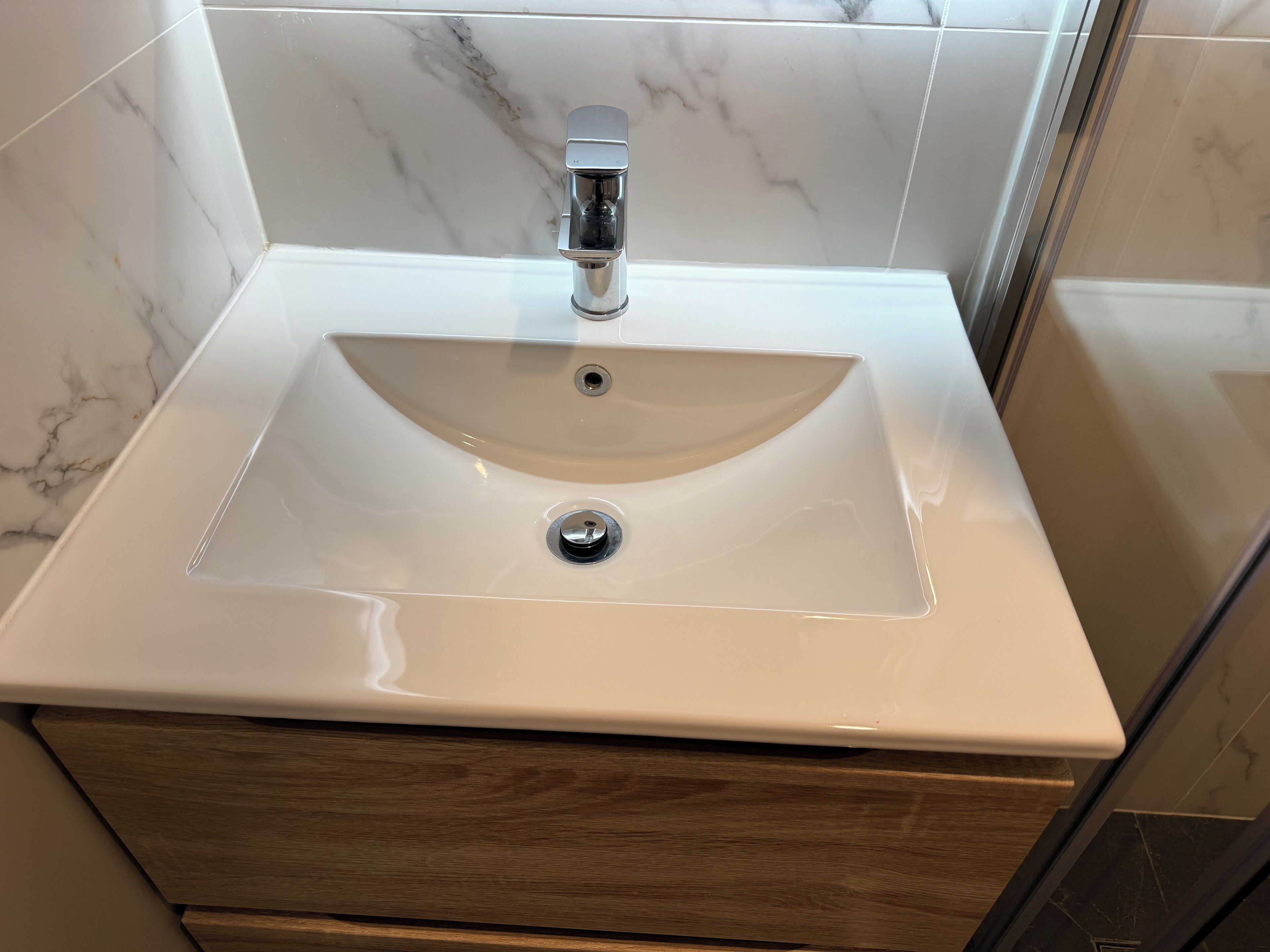 Un baño con lavamanos de mármol blanco, grifo cromado y cajón de madera debajo.