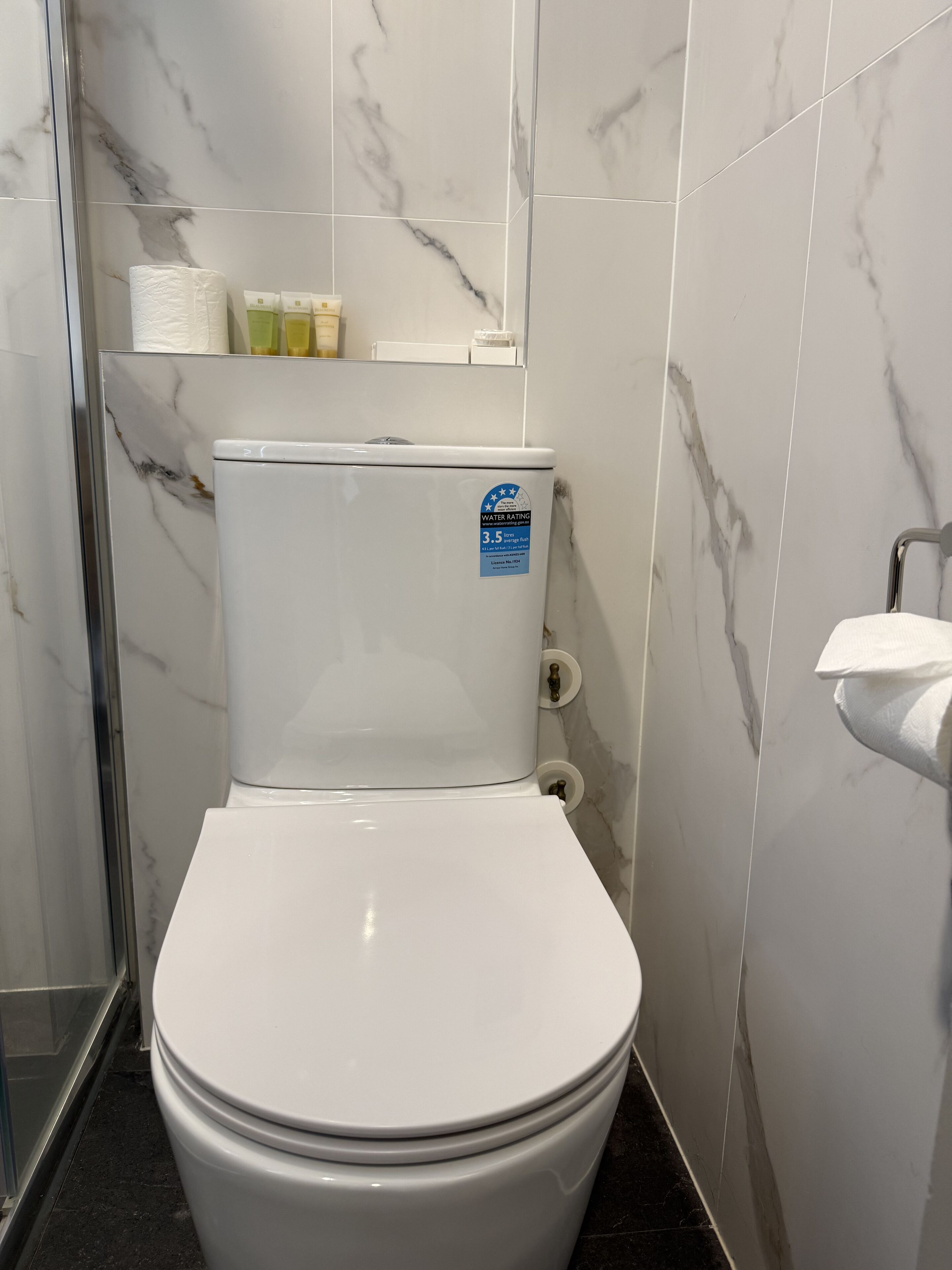 Un baño con inodoro blanco, paredes con diseño de mármol y zona de ducha.