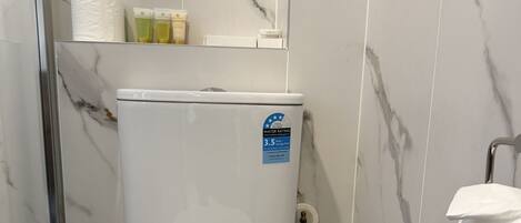 Un baño con inodoro blanco, paredes con diseño de mármol y zona de ducha.