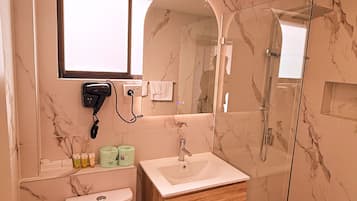 A modern bathroom with a marble backsplash, a white sink, a wooden vanity, a glass shower enclosure, and a toilet.