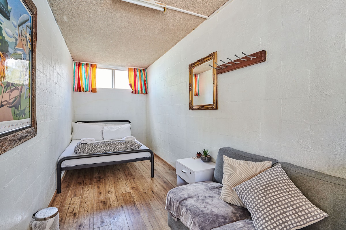A bedroom with a bed, a nightstand, a sofa, a window with curtains, and a mirror on the wall.